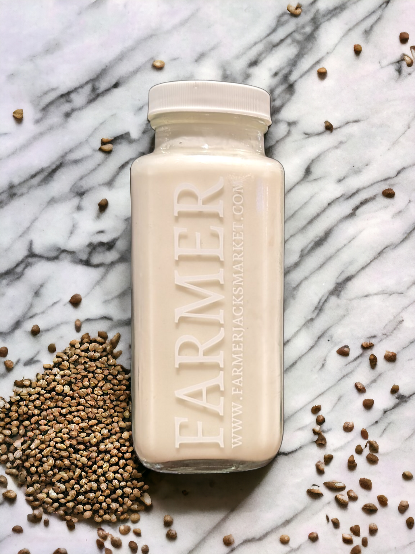 A rectangular glass bottle of white hemp milk against a marble backdrop with hemp seeds scattered around it.